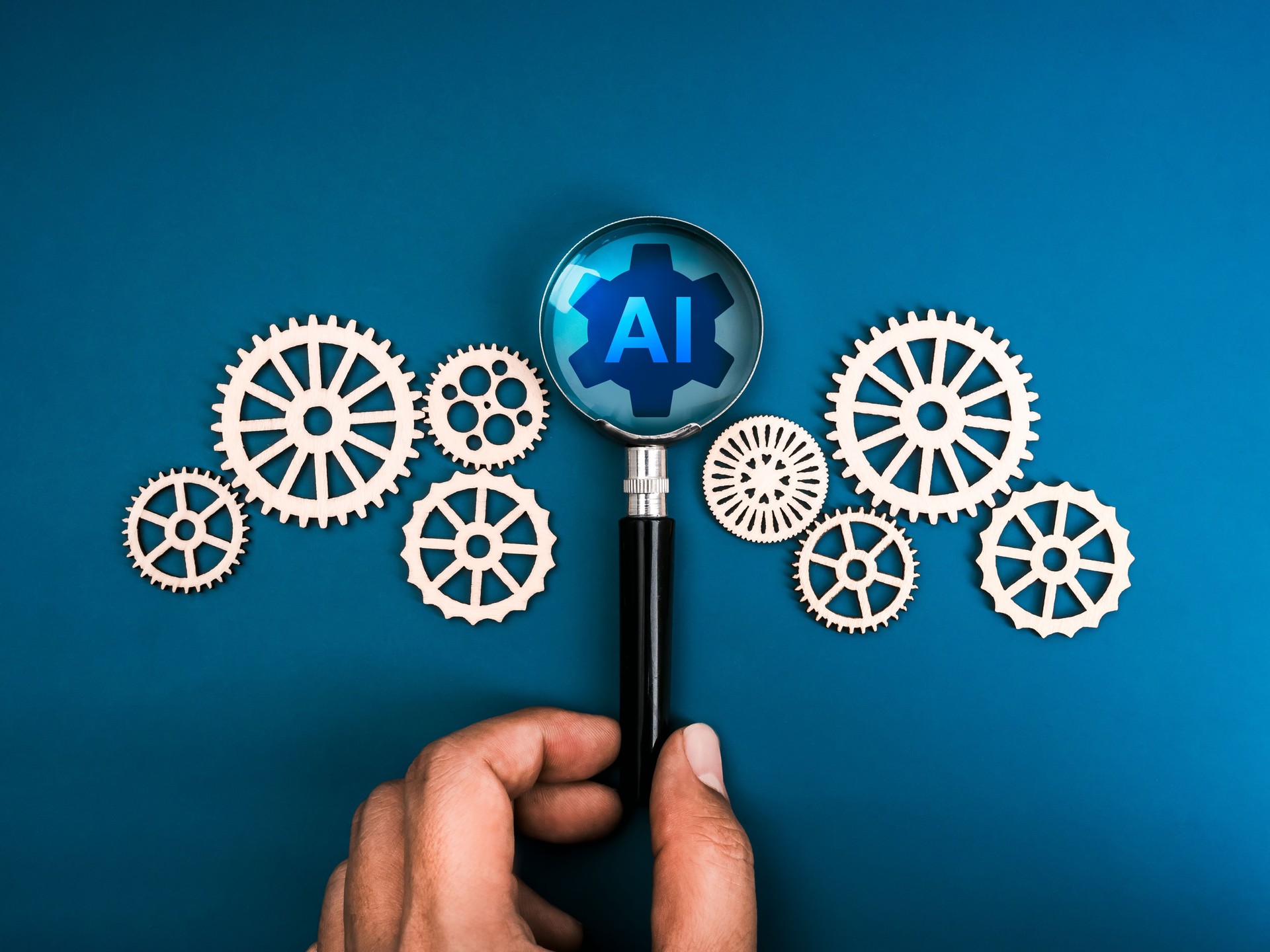 AI searching management tools, development technology assistance service support concept. AI mechanic gear icon in magnifying glass lens in human hand with many cogwheels, on blue background.